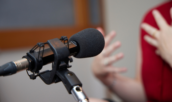 Microphone on a stand pointed towards a woman wearing red speaking and gesturing with her hands