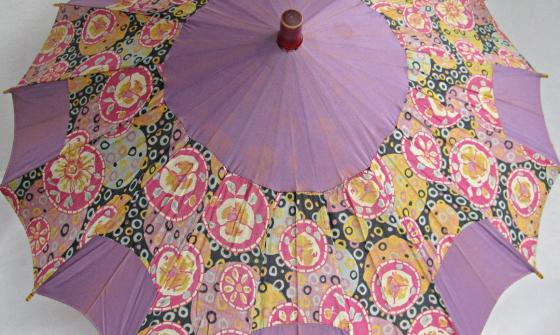 A vintage silk women's umbrella or parasol, which is opened and has alternating panels of mauve and floral design.