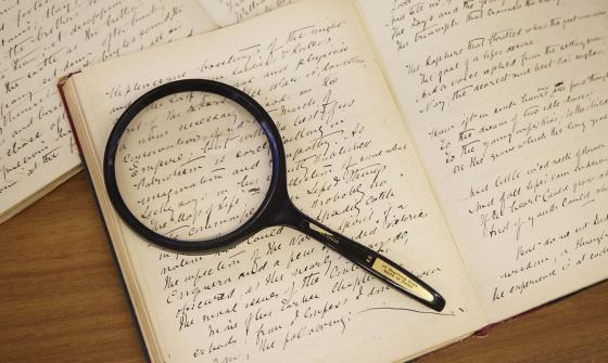 A magnifying glass sits on an old book with handwriting in it
