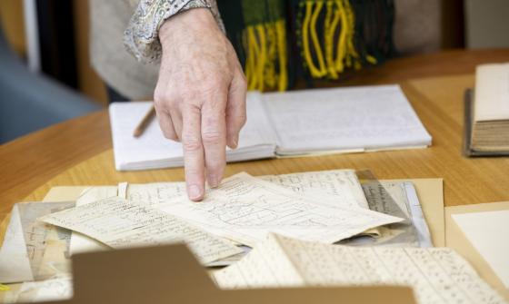 Woman's hand pointing at something on a map on a table with various manuscript material