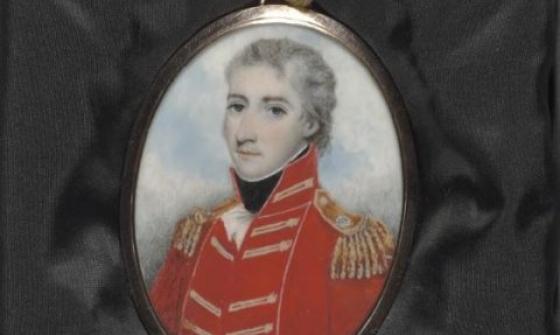 A painted locket portrait of a man in a red military uniform. The locket is resting on some black material.