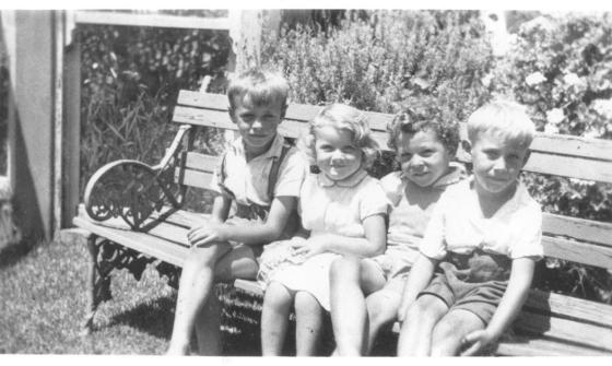 Four young children sitting on a bench and smiling