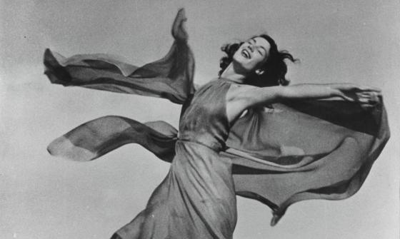 A black and white photograph of a woman in a dress twirling around with her eyes closed.