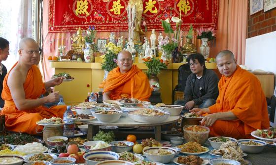 Three Buddhist Monks in orange robes sitting around a large spread of food in a temple