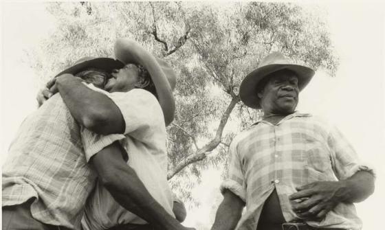 Two men hug and another man shakes one of their hands