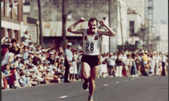 A marathon runner smiles and holds his fists up as he runs