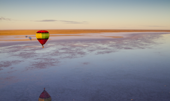 Hot air balloon flying over a huge lake and desert area that stretches out towards the horizon at dawn 