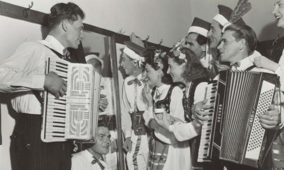 Group of men and women wearing traditional Polish clothing playing various instruments and smiling