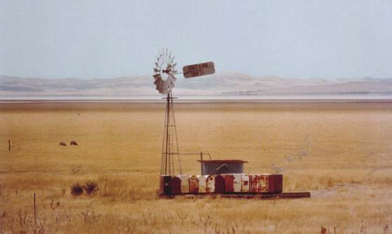 A windmill stands in a paddock surrounded by dry, yellow grass. Lake George in New South Wales is visible in the background.