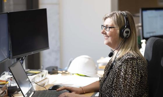 A smiling woman wearing headphones and typing on a computer