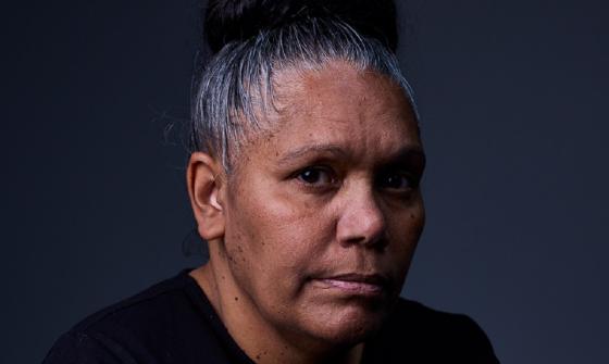 A portrait photo of a woman with her hair tied up in a bun and wearing a black shirt.