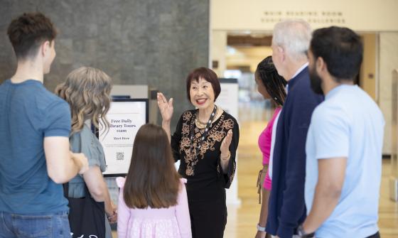 Volunteer Library tour guide smiling and greeting a tour group, made up of people of various ages, in the foyer.
