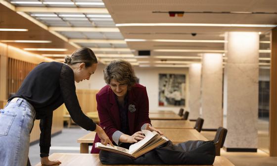 Two people bending over a desk and looking at a book.