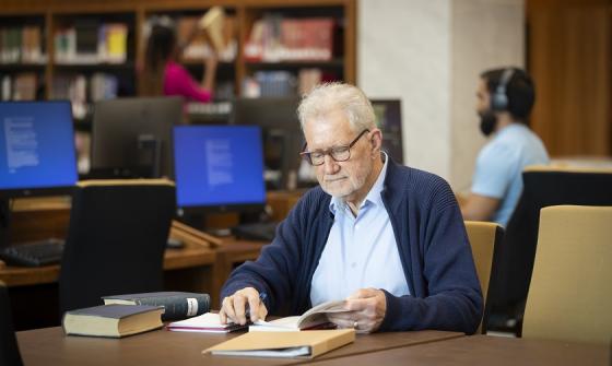 Man sitting at a table in the Main Reading Room reading a book with a notebook and pen nearby