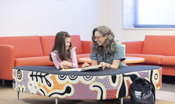 Woman and child smiling as they read a book in the kid's corner of the main reading room