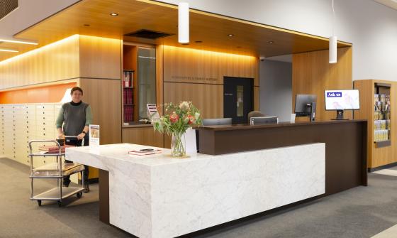 Librarian wheeling a trolley with collection material around the Newspapers & Family History Zone desk