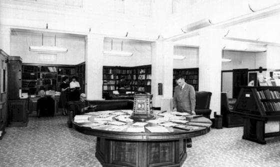 Several people in the Parliamentary Reading Room. One man is looking down at documents on a round table.