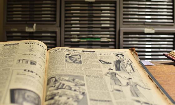An old volume is open on a table - illustrations and text can be seen on its pages.