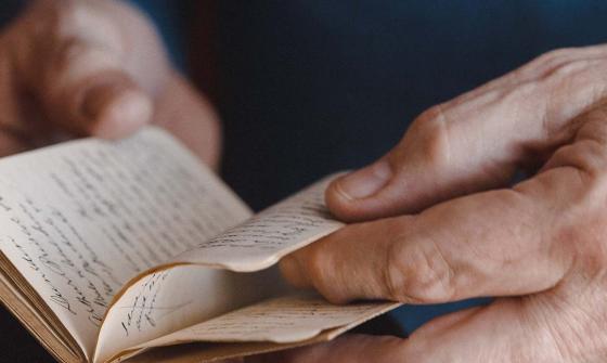 Close-up of a person's hands carefully turning the pages of an old, handwritten journal.