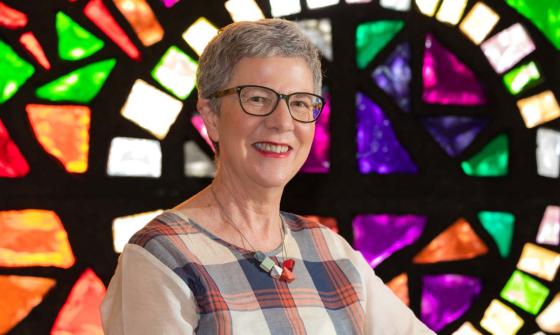 A woman with short hair smiles with stained glass windows in the background
