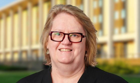 Woman with short blonde hair and dark red square glasses standing in front of the National Library