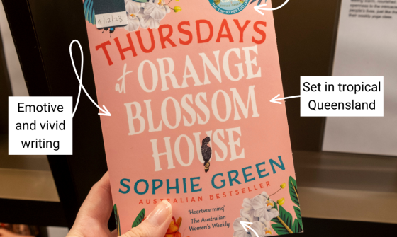 Pink book with floral imagery and text reading 'Thursdays at Orange Blossom House' and 'Sophie Green' being held up in front of a book display. Annotations surrounding the book read 'warm feelings', 'emotive and vivid writing', 'set in tropical Queensland' and 'friendship and family'