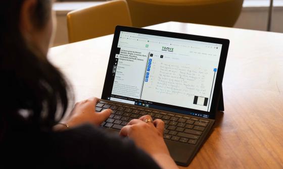 Over the shoulder of woman using laptop. On her screen she is using Trove to look at digitised handwritten notes from a lecture