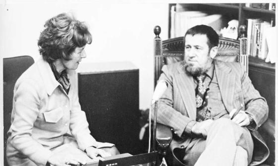 A woman sitting talking to a man while using a recorder.
