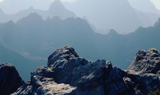 A sweeping landscape of a mountain range. The mountains are craggy and rocky. They are covered in mist.
