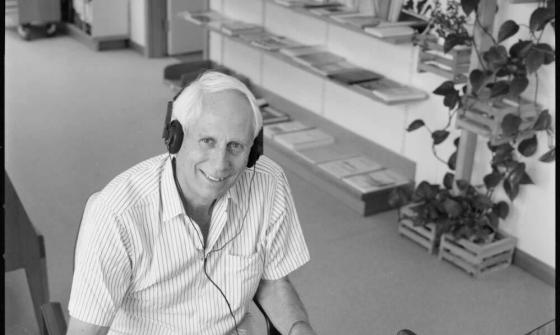Black and white photo of a man listening to a recording with a pen in hand and a piece of paper next to him
