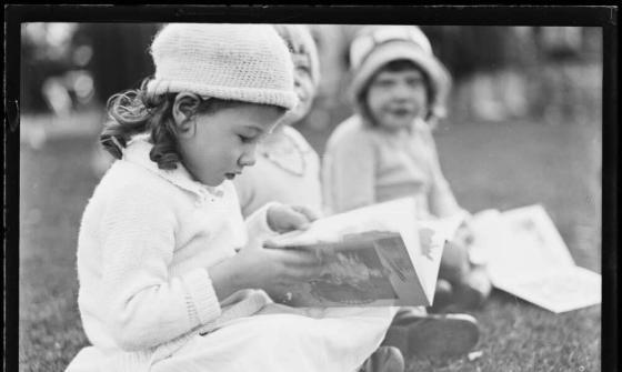 black and white photo of two girls sitting on the ground, wearing white and reading books