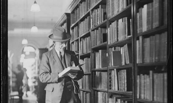 black and white photo of a man reading a book in a library