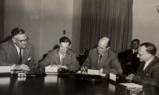 Four men seated at a table and one man sitting behind them