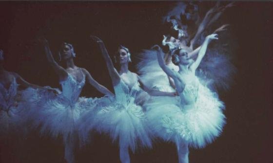 Three ballerinas mid-movement in matching white tutus