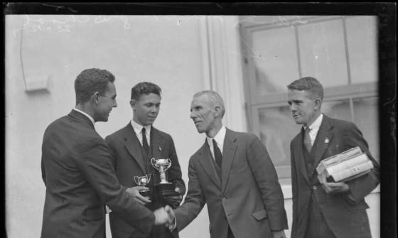 black and white photo of two men shaking hands while two schoolboys look on