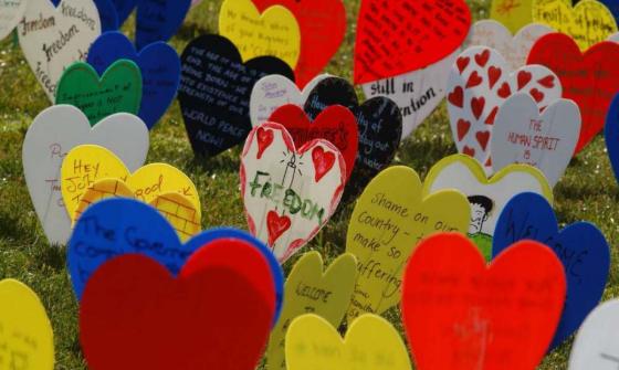 A photo of lots of different coloured plastic love hearts on a wire, stuck in a grassy area. The hearts are decorated with writing about freedom, and drawings.