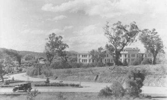 Black and white photo of a white building surrounded by trees and roads
