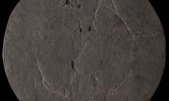 Image of a pock marked copper plate with writing inscribed across it from top to bottom.