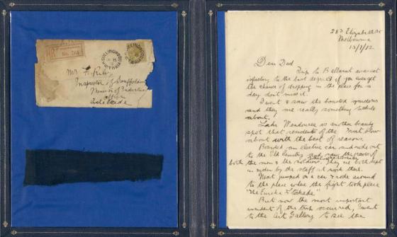 Display of an old stained, sepia coloured envelope, a sepia coloured letter and a portion of the Eureka stockade flag.