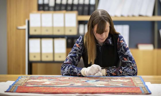 A woman wearing white gloves examining an item with a magnifying glass 