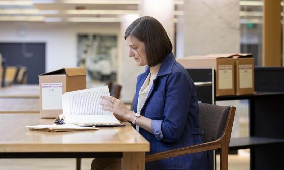 A woman turning the page in a book while sitting at a desk
