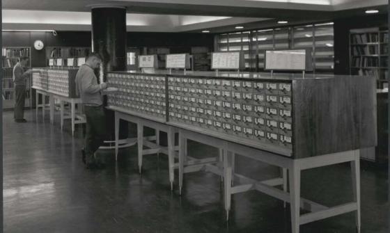 black and white photo of a man searching through a library card catalogue