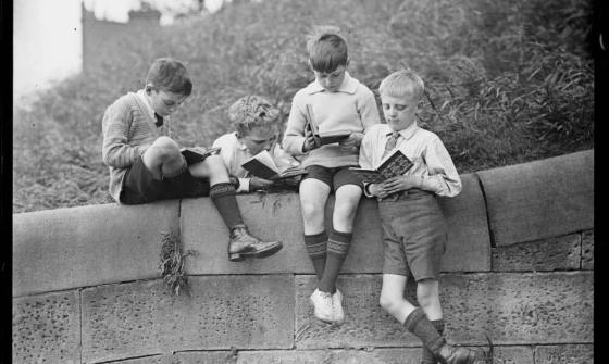 Four boys sitting on a stone wall and reading books