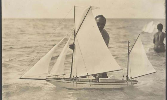 sepia photo of a man standing in water with a model boat