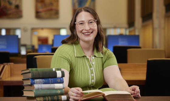 Zoe Smith, an NLA Scholar, sitting at a table in the Main Reading Room with a pile of books and smiling