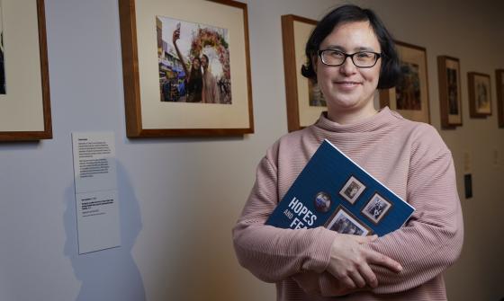 Exhibition curator standing in the Hopes and Fears exhibition gallery holding the exhibition book and smiling