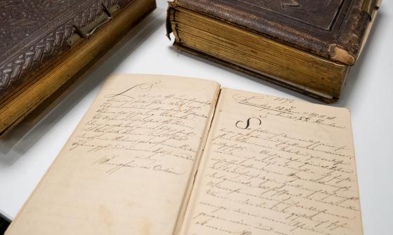 Three leatherbound diaries from the nineteenth century, one open showing neat handwriting