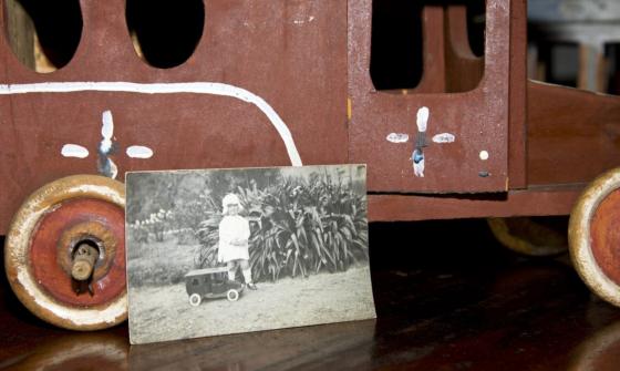 Black and white photo of a child with a toy car, leaning against the real toy car