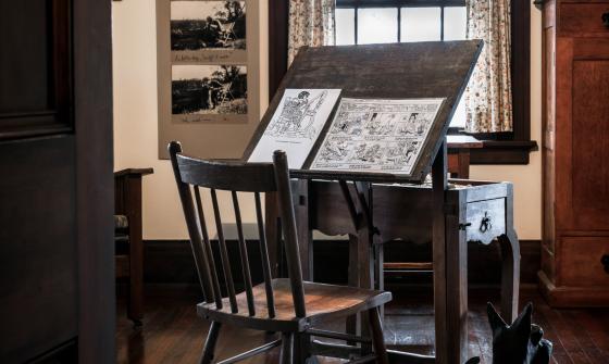 Easel, with two illustrated pages on it, and chair in May Gibbs' studio in Nutcote