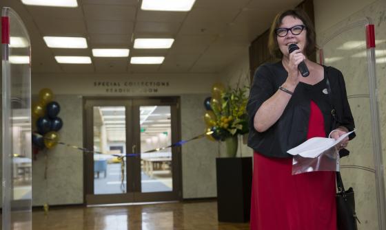 Woman, Margaret Burn, standing with a microphone in front of the Special Collections Reading Room, the opening of which is decorated with ribbons and balloons